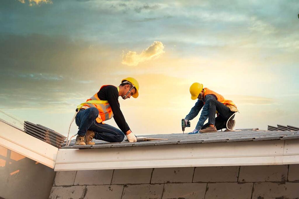 A person wearing safety gear and non-slip shoes walking on a residential shingle roof with a blue sky above.