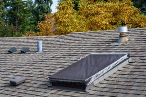 A contractor installing new shingles on a residential roof under a partly cloudy sky.