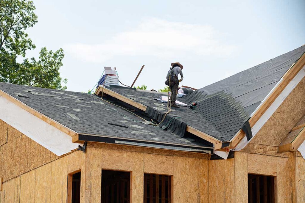 A person holding a sample shingle up to an existing roof to compare colors and textures.