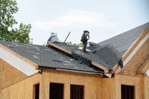 A person holding a sample shingle up to an existing roof to compare colors and textures.