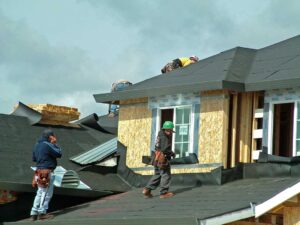 Homeowner inspecting roof shingles from a ladder with gloves, flashlight, and soft brush nearby