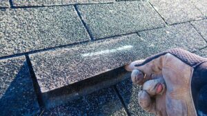 Roofing workers inspect exposed roof decking beside stacked materials on a residential house.