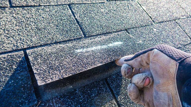 Roofing workers inspect exposed roof decking beside stacked materials on a residential house.